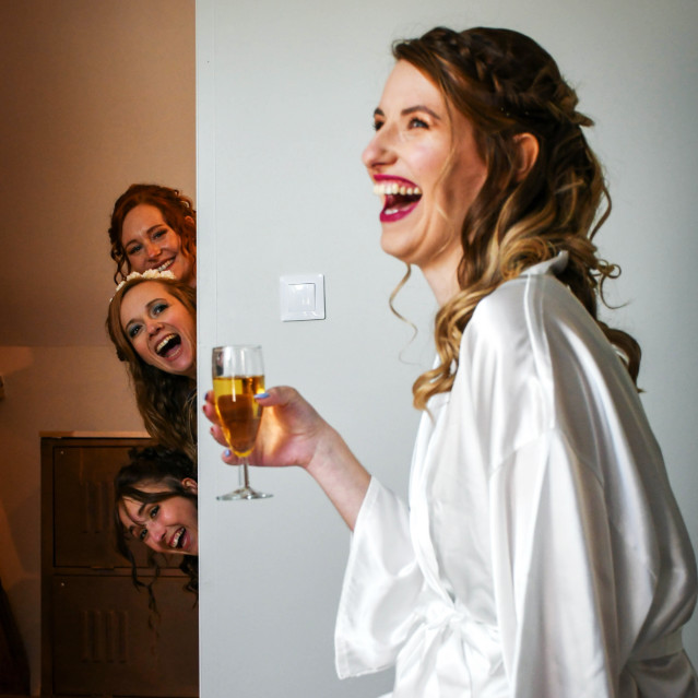 Future mariée entrain de rire avec verre champagne à la main - En fond demoiselles d'honneurs qui rient